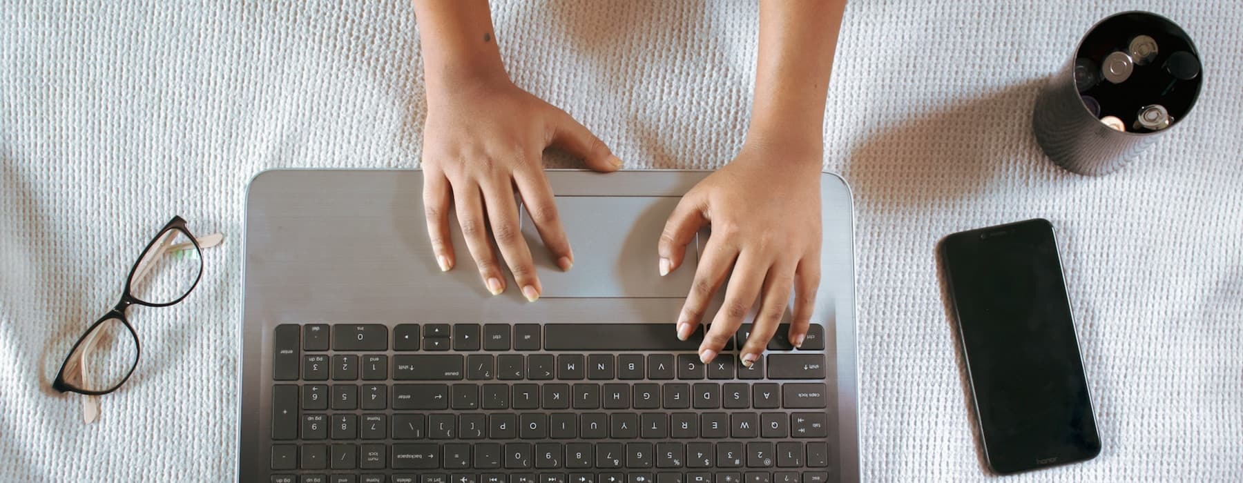 lifestyle image of a person's hand typing beside a cup of coffee